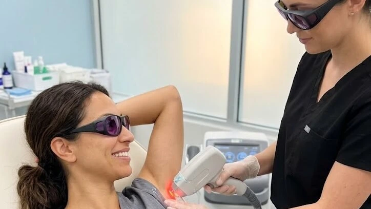 A practitioner treating a client underarm with a laser handpiece, both wearing protective eyewear.